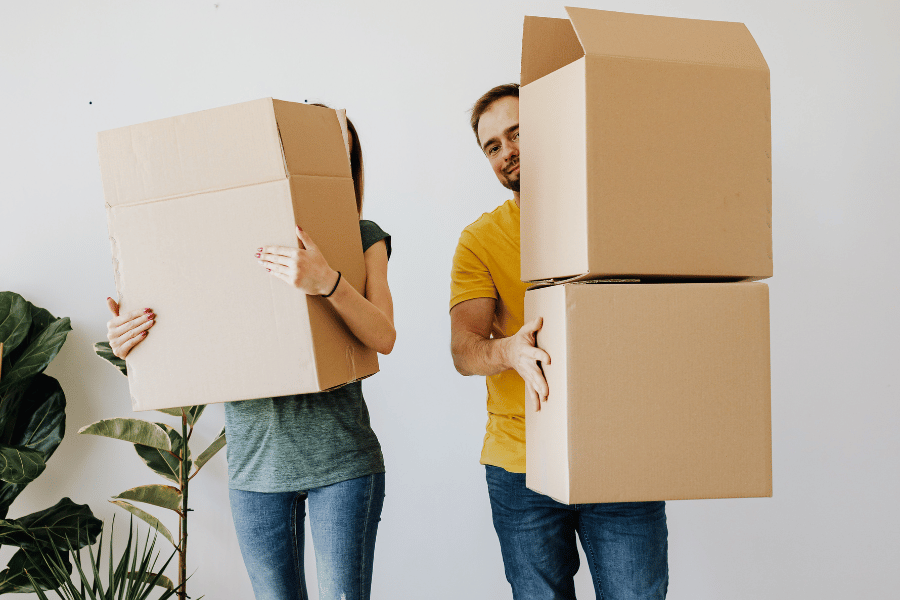couple holding cardboard moving boxes in their home