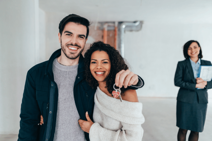 happy homebuyer couple holding the keys to their new home while the real estate agent stands in the background