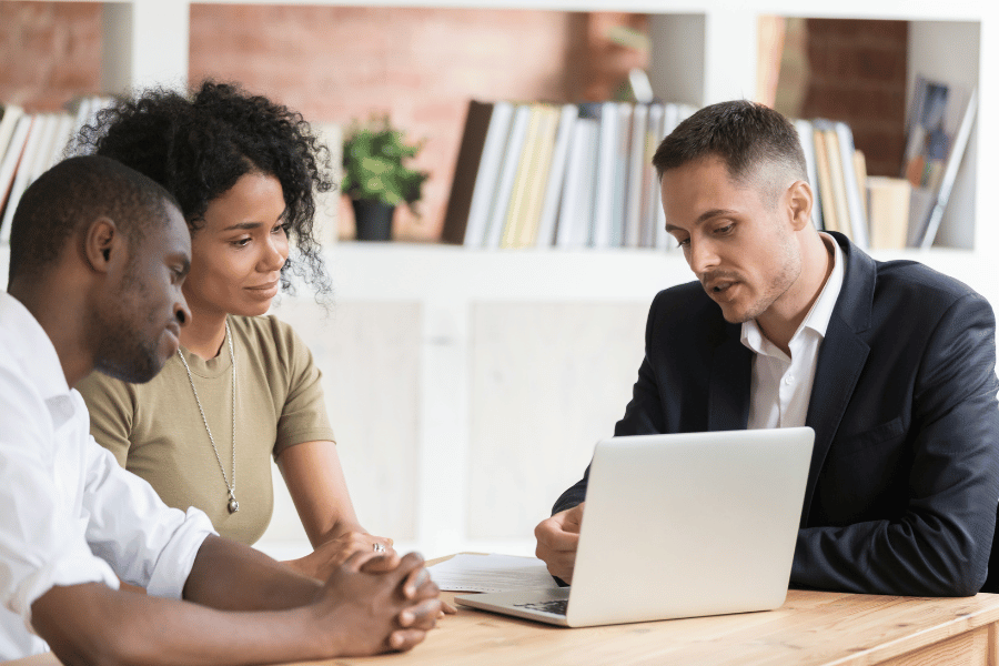 Real estate agent sitting down with clients and working on a computer discussing home options